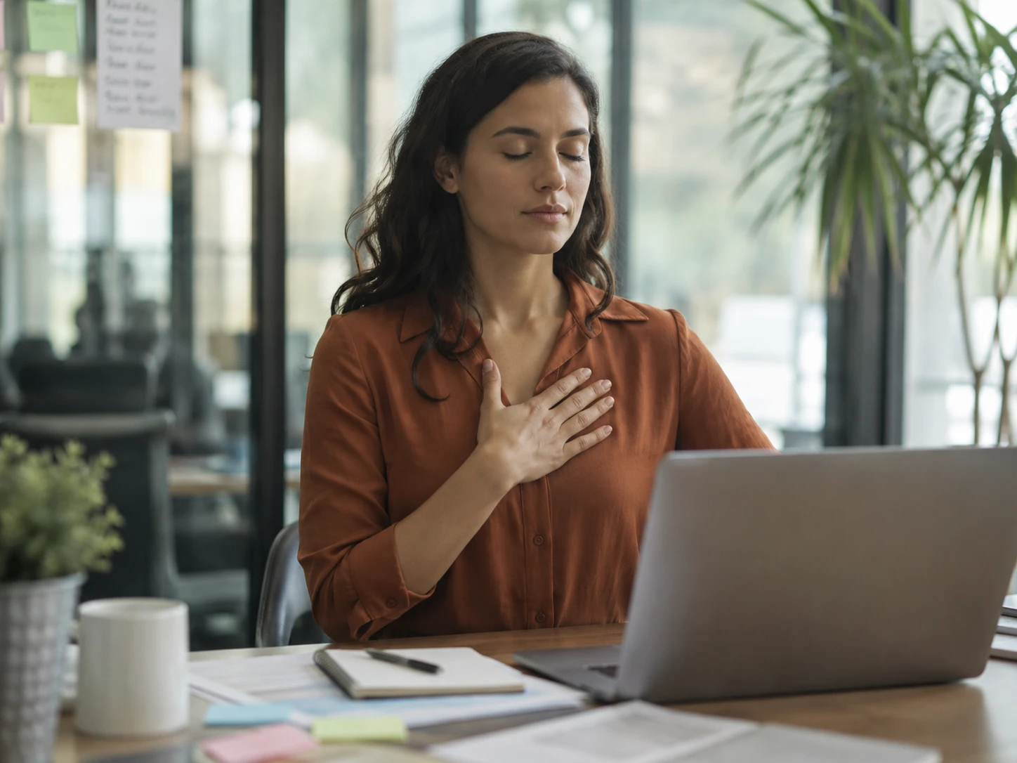 Mujer con los ojos cerrados meditando frente al computador, llevando la práctica de autoobservación a su día laboral